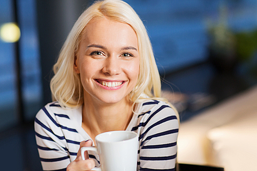 leisure, drinks, people and lifestyle concept - smiling young woman drinking coffee or tea at cafe