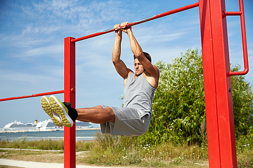 fitness, sport, exercising, training and lifestyle concept - young man doing abdominal exercise on horizontal bar in summer park