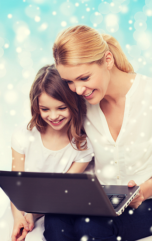 family, childhood, holidays, technology and people concept - smiling mother and little girl with laptop computer over blue background with snow