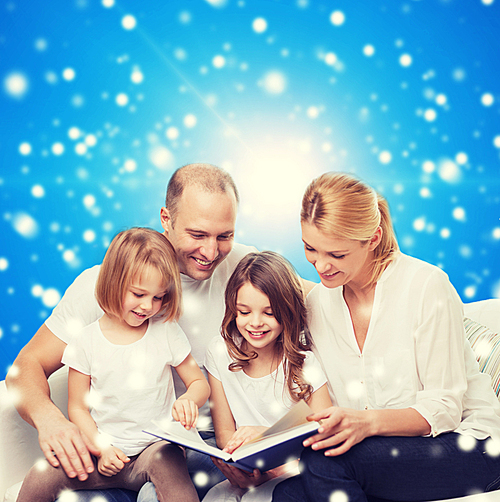 family, childhood, christmas holidays and people - smiling mother, father and little girls reading book over blue snowy background