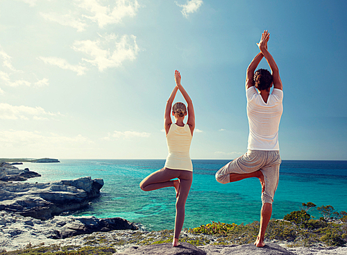 fitness, sport, and lifestyle concept - couple making yoga exercises on beach from back