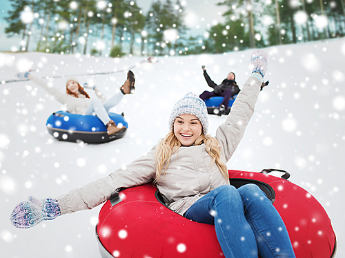 winter, leisure, sport, friendship and people concept - group of happy friends sliding down on snow tubes