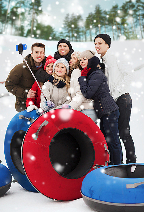 winter, leisure, sport, friendship and people concept - group of smiling friends with snow tubes taking picture by smartphone selfie stick outdoors