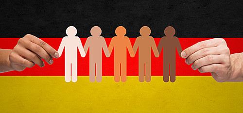 community, unity, population, race and humanity concept - multiracial couple hands holding chain of paper people pictogram over german flag background