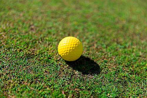 game, entertainment, sport and leisure concept - close up of yellow golf ball on green field grass