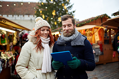 holidays, winter, christmas, technology and people concept - happy couple of tourists in warm clothes with tablet pc computer walking in old town