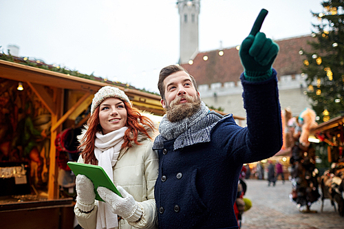 holidays, winter, christmas, technology and people concept - happy couple of tourists in warm clothes with tablet pc computer pointing finger in old town