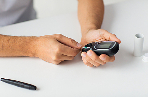 medicine, diabetes, glycemia, health care and people concept - close up of man checking blood sugar level by glucometer at home