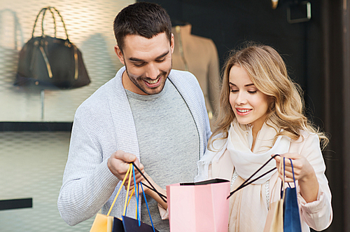 sale, consumerism and people concept - happy couple looking into shopping bag at shop window in city