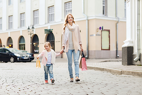 sale, consumerism and people concept - happy mother and child with shopping bags walking along city street