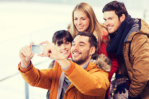 people, friendship, technology and leisure concept - happy friends taking selfie with digital camera on skating rink