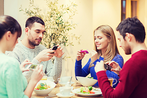 people, leisure, friendship and technology concept - group of happy friends with smartphones taking picture of food at cafe