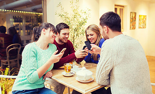 people, leisure, friendship and technology concept - group of happy friends with smartphones meeting at cafe and drinking tea