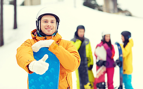 winter, leisure, extreme sport, friendship and people concept - happy young man in helmet with snowboard and group of friends showing thumbs up