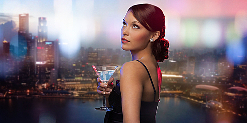 party, drinks, holidays, luxury and celebration concept - smiling woman in evening dress holding cocktail over night city background