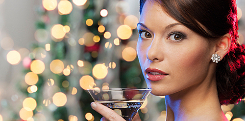 party, drinks, holidays, luxury and celebration concept - woman face with cocktail over christmas tree lights