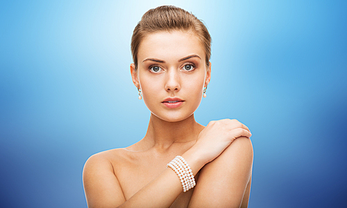 beauty, luxury, people, holidays and jewelry concept - beautiful woman with pearl earrings and bracelet over blue background