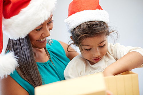 christmas, holidays, family, childhood and people concept - happy mother and little girl in santa hats opening gift box at home