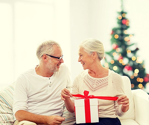 family, holidays, age and people concept - happy senior couple with gift box over living room and christmas tree background