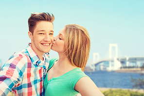 travel, tourism, technology, love and people concept - smiling couple kissing and taking selfie over  bridge in tokyo and river background