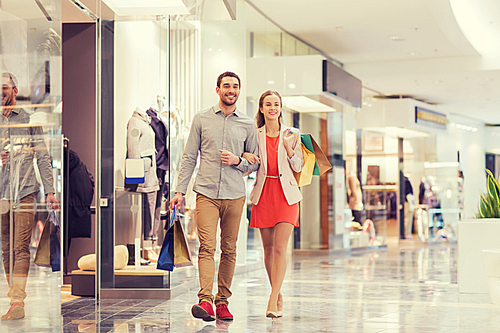 sale, consumerism and people concept - happy young couple with shopping bags walking in mall