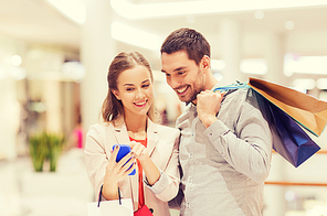 sale, consumerism, technology and people concept - happy young couple with shopping bags and smartphone talking in mall