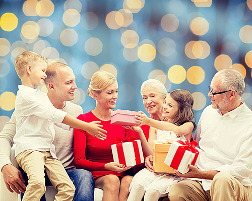 family, holidays, generation, christmas and people concept - smiling family with gift boxes sitting on couch over blue lights background