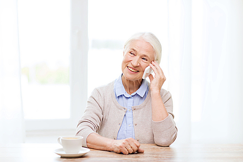 technology, communication age and people concept - happy senior woman with smartphone and coffee sitting at table and calling at home