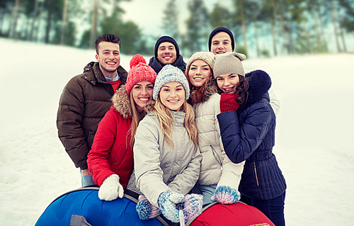 winter, leisure, friendship, technology and people concept - group of smiling young men and women with snow tubes taking picture with smartphone selfie stick outdoors