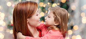 family, holidays, children and people concept - happy mother and little daughter hugging over christmas tree lights background