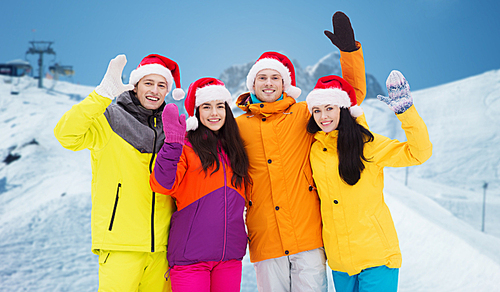 winter holidays, christmas, friendship and people concept - happy friends in santa hats and ski suits over downhill skiing and mountains background