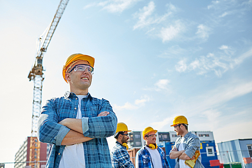 business, building, teamwork and people concept - group of smiling builders in hardhats at construction site