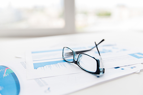 business, objects and statistics concept - close up of eyeglasses and files on office table