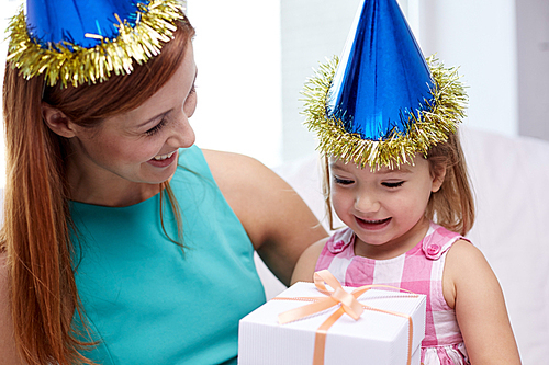 holidays, birthday family, childhood and people concept - happy mother and little girl in party caps with gift box at home