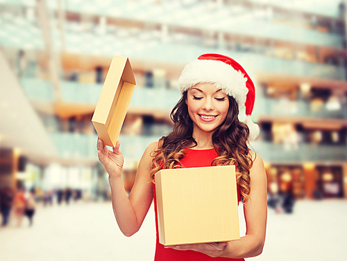 christmas, holidays, celebration and people concept - smiling woman in santa helper hat with gift box over shopping center background