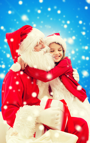 holidays, christmas, childhood and people concept - smiling little girl hugging with santa claus over blue snowy background
