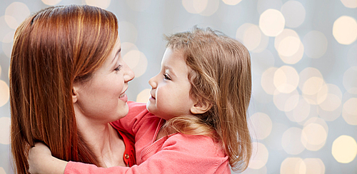 family, children and people concept - happy mother and little daughter hugging over holidays lights background