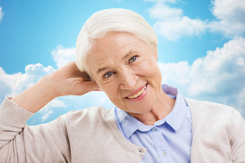 age and people concept - happy smiling senior woman over blue sky and clouds background