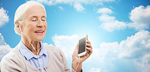 technology, age and people concept - happy senior woman with smartphone and earphones listening to music over blue sky and clouds background