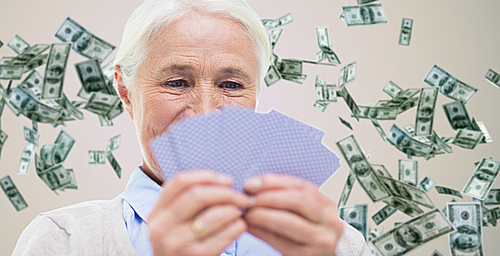 age, game, gamble, poker and people concept - close up of happy smiling senior woman playing cards over dollar money rain on background