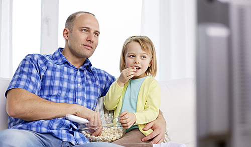 family, children, parenthood people concept - happy father and daughter eating popcorn and watching tv at home