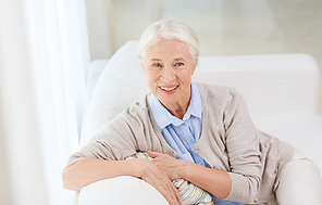 age and people concept - happy smiling senior woman sitting on sofa at home