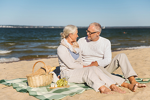 family, age, travel, tourism and people concept - happy senior couple having picnic and talking on summer beach