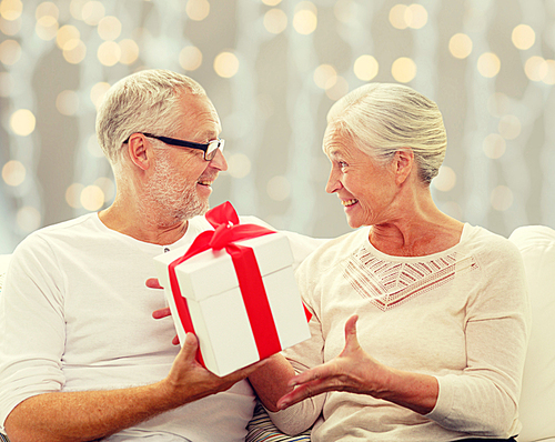 family, holidays, christmas, age and people concept - happy senior couple with gift box over holidays lights background