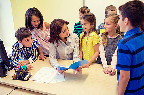 education, elementary school, learning and people concept - group of school kids with teacher talking in classroom