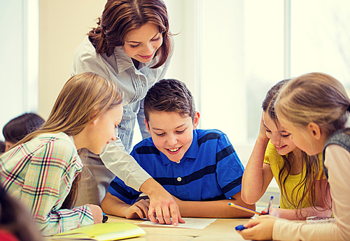 education, elementary school, learning and people concept - teacher helping school kids writing test in classroom