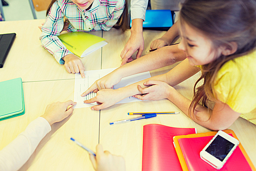 education, elementary school, learning and people concept - close up of school kids pointing fingers to paper with test on desk at classroom