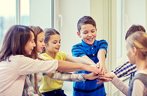 education, elementary school, children, break and people concept - group of smiling school kids putting hands on top in corridor