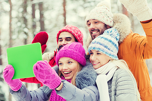 technology, season, friendship and people concept - group of smiling men and women taking selfie tablet pc computer in winter forest