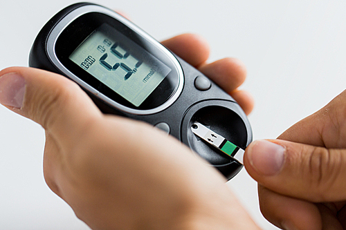 medicine, diabetes, glycemia, health care and people concept - close up of man checking blood sugar level by glucometer and test stripe at home